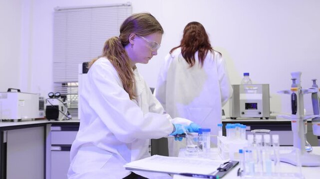 Female scientist pipetting liquid into a test tube and writing down results on a clipboard.