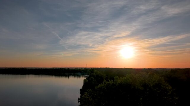 Sunset aerial panorama over Mittellandkanal in Saxony-Anhalt, Germany, with glowing water winding through flat countryside. Warm evening light reveals farmland, forest, horizon and distant turbines