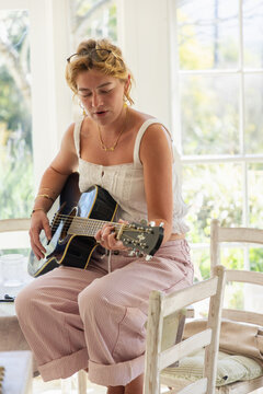 stylish young woman playing guitar in light filled room