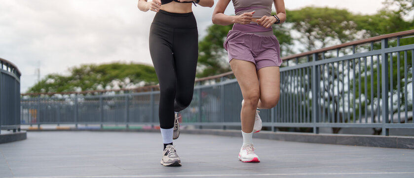 Cropped view of two women running outdoors for cardio fitness and workout routine