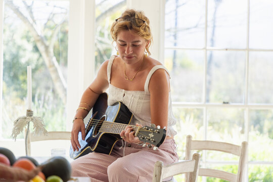 stylish young woman playing guitar in light filled room