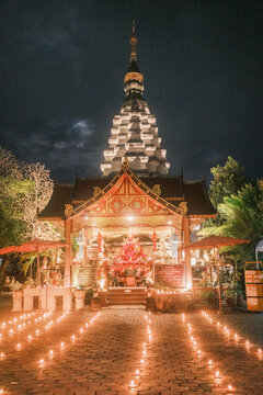 View of the illuminated Wat Chedi Luang temple at night with rows of glowing candles on the stone path, Chiang Mai, Thailand.