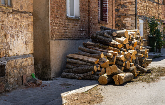 View of a large pile of stacked firewood logs resting against a rustic brick and stone wall in the historic village of Vevchani, Vevcani Municipality, North Macedonia.
