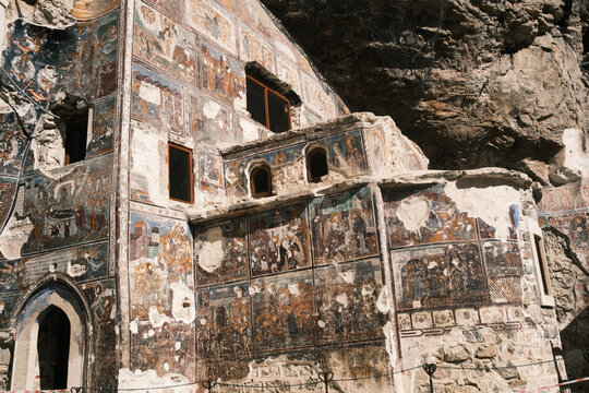View of the historic Sumela Monastery built into the cliffside, featuring intricate religious frescoes on its exterior walls, stone architecture, and arched windows in Macka, Trabzon, Turkiye.