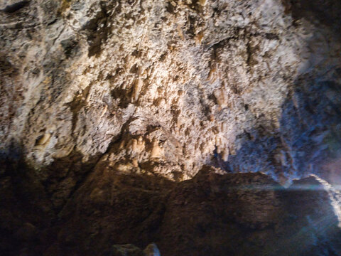 Massive limestone cave interior showcasing intricate textured rock formations with natural stalactites hanging from a dark rugged ceiling illuminated by mysterious soft light in underground cavern