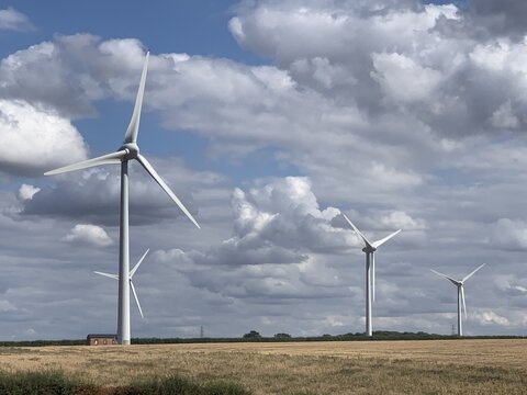 View of Burton Wold wind farm with large white wind turbines standing in a golden wheat field under a cloudy blue sky in Burton Latimer, England, United Kingdom.