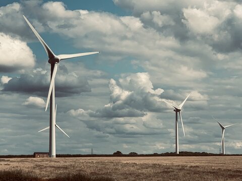 View of wind turbines at Burton Wold wind farm set against a cloudy sky over a harvested field in Burton Latimer, England, United Kingdom.