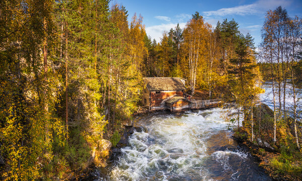 View of the historic Myllykoski mill situated by the rushing rapids of the Oulanka River, surrounded by vibrant autumn foliage in Oulanka National Park, Kuusamo, Finland.