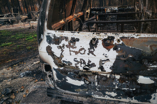 View of a burnt-out van with the words For Sale written on the side, surrounded by charred trees and fire-damaged landscape in Spokane, Washington, United States.