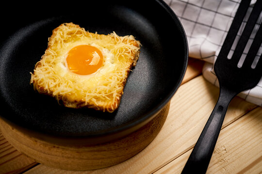 Delicious toast with fried egg in pan on wooden kitchen table