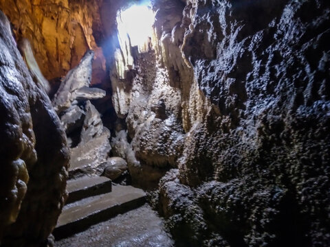Majestic underground cave formations display intricate limestone stalactites and rough stone textures illuminated by dramatic lighting within this deep cavern passage during a peaceful tourist 