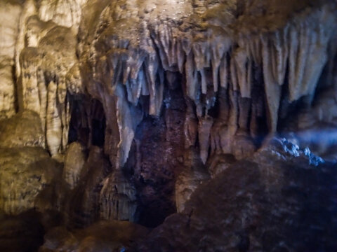 Massive limestone stalactites hanging from the dark rugged ceiling inside a deep subterranean cavern create a textured natural display captured with soft ambient interior lighting