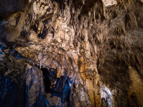 Limestone stalactites and stalagmites hanging from the dark rugged cavern ceiling creating beautiful geological rock formations inside this deep natural underground mountain cave adventure spot