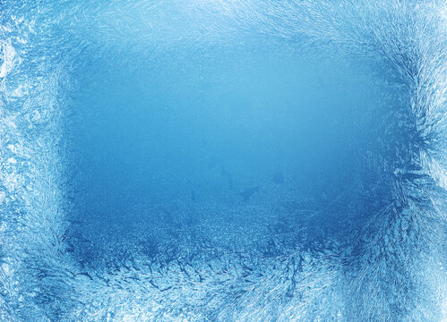 Full frame blue icy frost texture background with dense frozen winter patterns on glass window with an empty blue space.