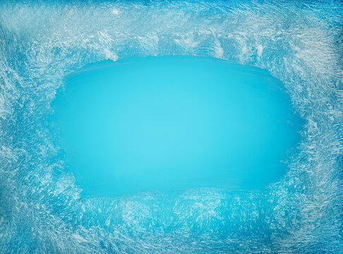 Blue icy frost texture background with dense frozen winter patterns on glass window with an empty blue space in the middle for seasonal backgrounds.