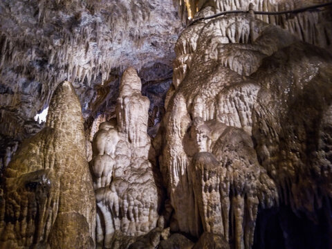 Massive stalactites and stalagmites formed inside a dark limestone cavern showcasing intricate geological textures with natural earthy tones illuminated by soft light in underground chambers
