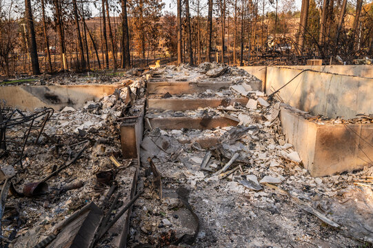 View of the charred remains of a building foundation with stone stairs surrounded by burnt trees following a wildfire in Spokane, Washington, United States.