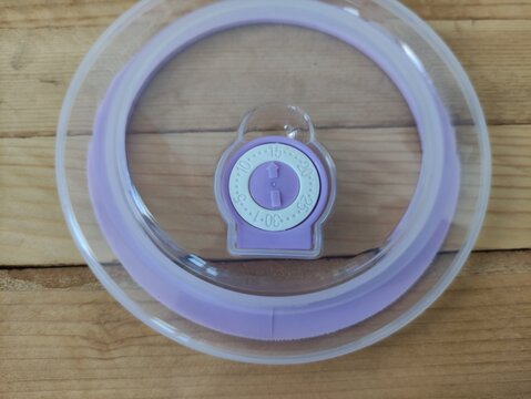 Purple and transparent plastic food container lid with date dial on wooden table