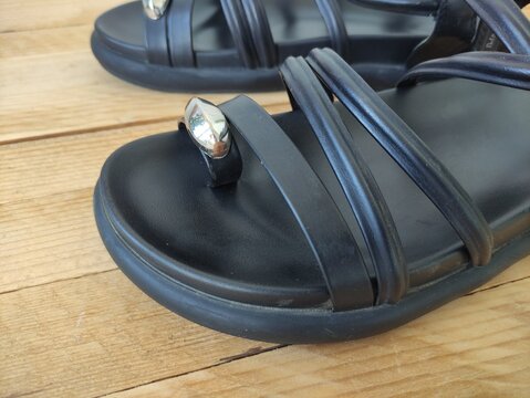 Close up of black sandal straps with silver ornament on a wooden floor