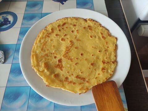 Large golden fried flatbread pancake served on a white plate with wooden spatula