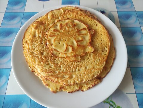 Stack of golden fried pancakes with a smaller pancake on top served on a white plate