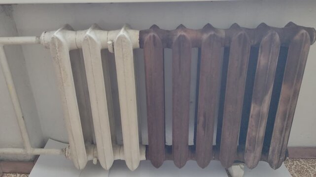 Old cast iron heating radiator with white and rusty brown sections near a window