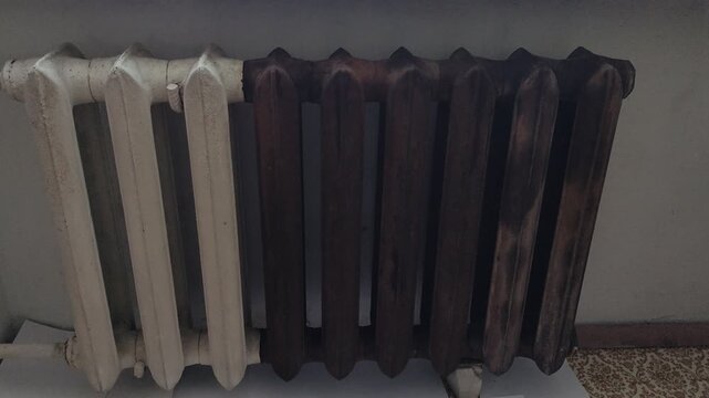Old cast iron heating radiator with white and rusty brown sections near a window