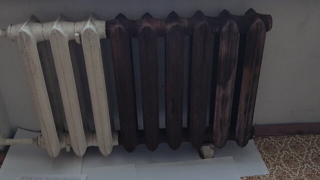 Old cast iron heating radiator with white and rusty brown sections near a window