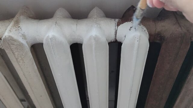 Person holding a paint brush and painting a cast iron radiator white, first person view video