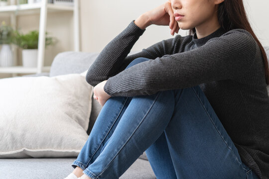 Unhappy anxiety young Asian woman covering her face with pillow on the cough in the living room at home.