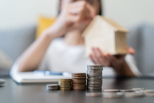 Close up stacking coins and hands of Woman putting coin into piggy bank house model  in the background