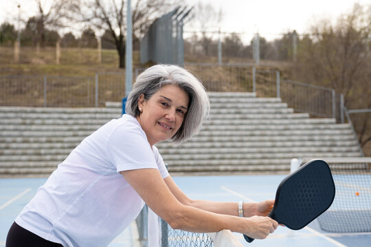 Senior woman standing on a pickleball court holding a paddle and smiling