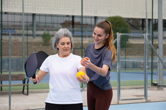 Senior woman learning pickleball from a coach on an outdoor court