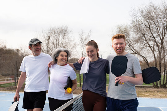 Happy pickleball players of different ages walking on a court after a game