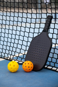 Pickleball paddle and two balls on a blue court against a black net