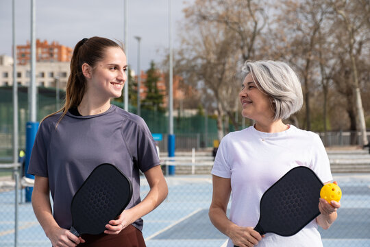 Women standing on a pickleball court, holding paddles and ball