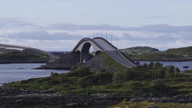 The iconic curved Storseisundet Bridge spans across coastal islets along the famous Atlantic Ocean Road under a cloudy sky in Norway.
