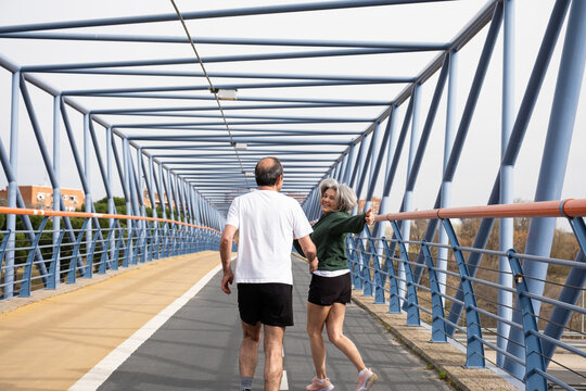 Happy senior couple jogging together on a modern bridge, staying active outdoors