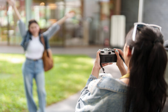 Asian woman taking photo of excited friend with open arms during travel vacation