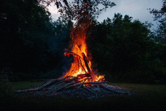 View of a large bonfire burning at night with bright orange flames and sparks rising into the dark sky against a backdrop of trees in Vormsi, Laane County, Estonia.
