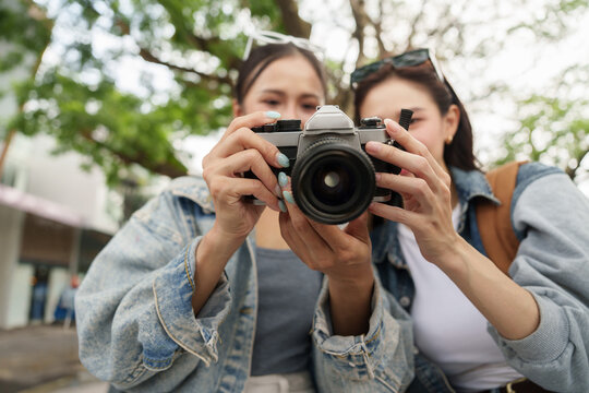 Two Asian female tourists taking photos with vintage camera during vacation trip