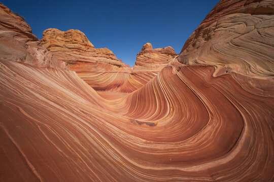 View of The Wave, a sandstone rock formation with swirling red and orange layers under a clear blue sky in Kanab, Arizona, United States.