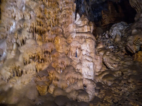 Ancient limestone cave stalactites and stalagmites showcasing intricate natural mineral formations with beautiful earth tones and dramatic shadows inside a dark deep underground mountain cavern system