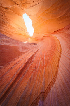 View of the swirling orange and red sandstone layers of The Wave, illuminated by natural light in the desert landscape of Kanab, Arizona, United States.