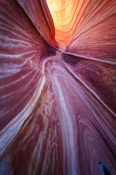 View of the swirling red and orange sandstone layers of The Wave, showcasing smooth rock textures and natural light in the desert landscape of Kanab, Arizona, United States.