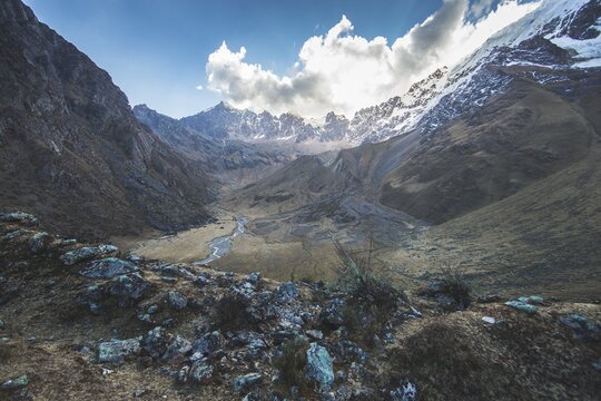 View of the snow-capped Salcantay mountain peak rising above a rugged valley with a winding river and rocky slopes in Urubamba Province, Cusco, Peru.