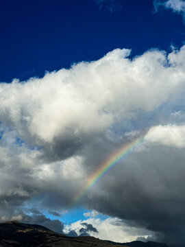 View of a vibrant rainbow arching across a dramatic cloudy sky above the rolling hills in Ashland, Oregon, United States.