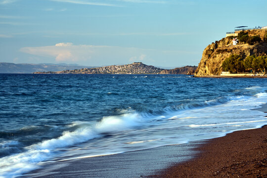 pebbly beach with umbrellas, windmill on a rock and view of Molyvos village on Lesbos island