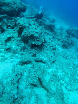 View of a scuba diver exploring an underwater ancient anchor on the rocky seabed in the clear blue waters near Kas, Antalya, Turkey.