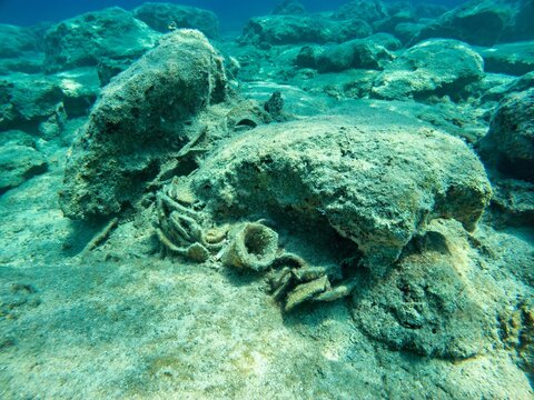 View of ancient pottery shards and amphorae fragments resting on the rocky seabed in the clear Mediterranean waters of Kas, Antalya, Turkey.